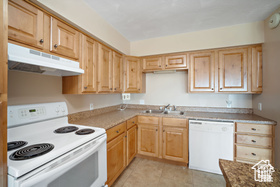 Kitchen featuring white appliances, under cabinet range hood, a sink, light brown cabinets, and light tile patterned floors