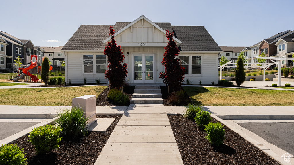View of front facade with french doors, a front yard, board and batten siding, and a residential view