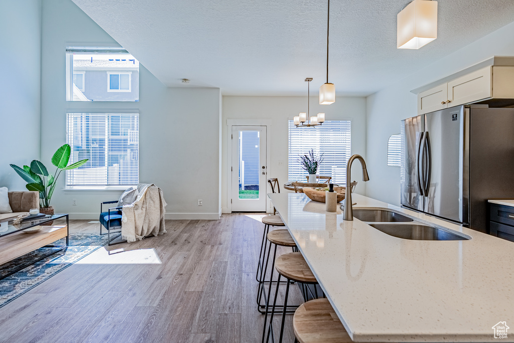Kitchen with freestanding refrigerator, light wood-style flooring, light stone counters, pendant lighting, and a textured ceiling