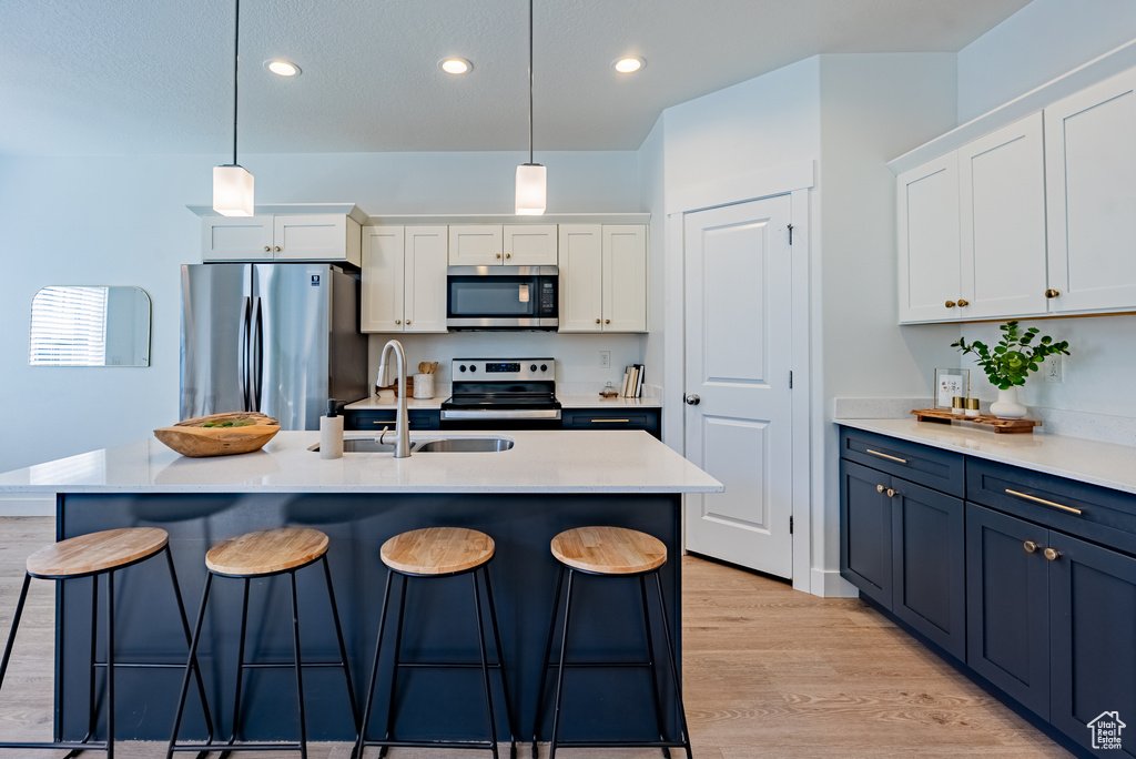 Kitchen with stainless steel appliances, a kitchen breakfast bar, white cabinets, light wood-style floors, and recessed lighting