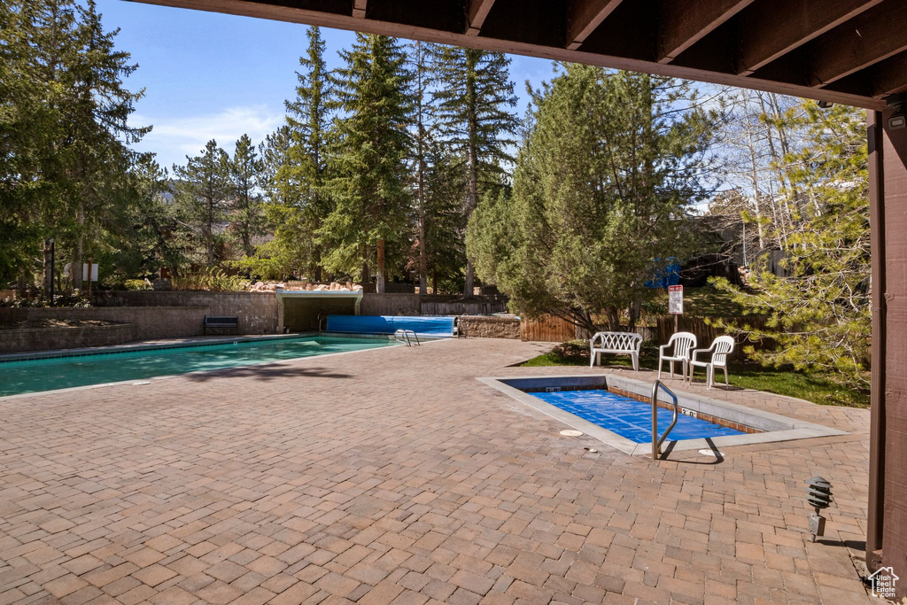 View of pool with a patio, view of scattered trees, and fence