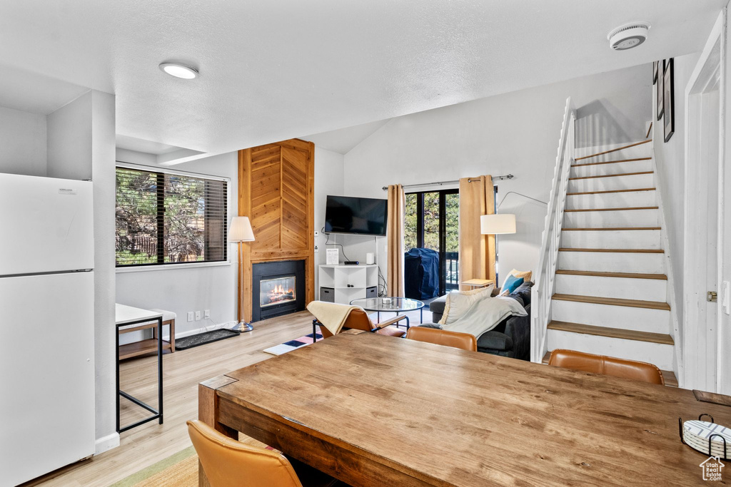Dining area featuring a fireplace, light wood-type flooring, stairway, vaulted ceiling, and baseboards