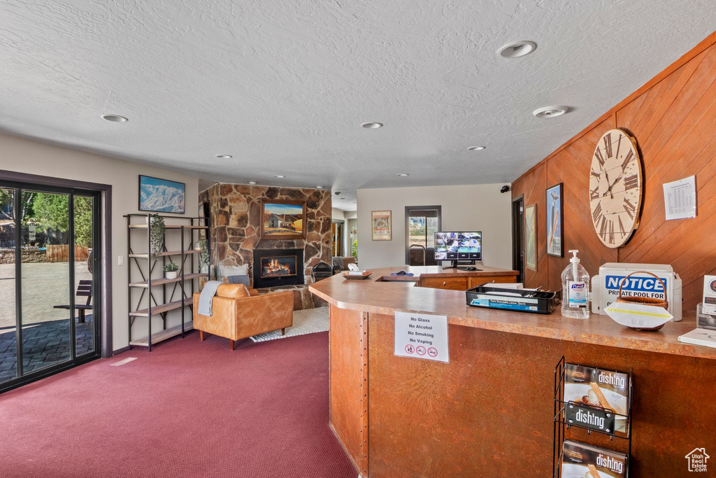 Kitchen featuring a textured ceiling, dark colored carpet, wood walls, a stone fireplace, and recessed lighting