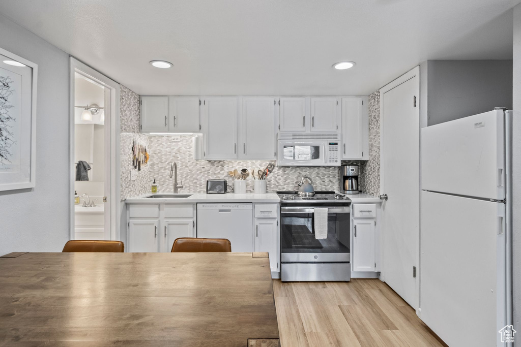 Kitchen featuring white appliances, a sink, white cabinets, light wood finished floors, and recessed lighting
