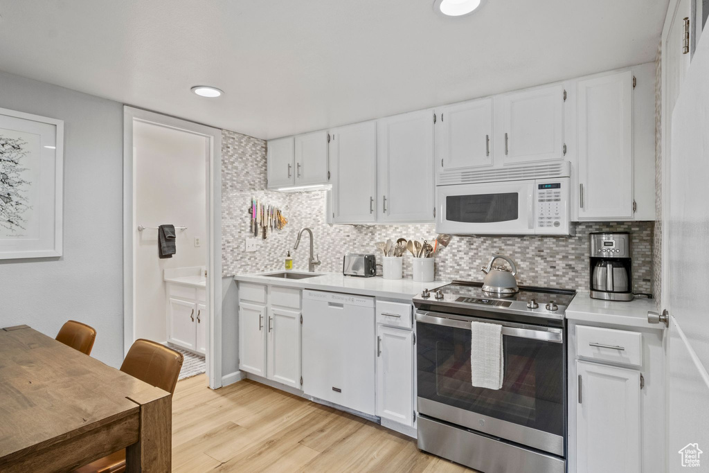 Kitchen featuring white appliances, a sink, light wood-style floors, white cabinets, and recessed lighting