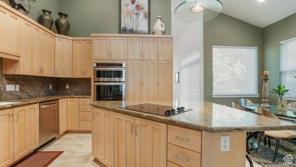Kitchen featuring light brown cabinets, appliances with stainless steel finishes, backsplash, a center island, and light stone counters
