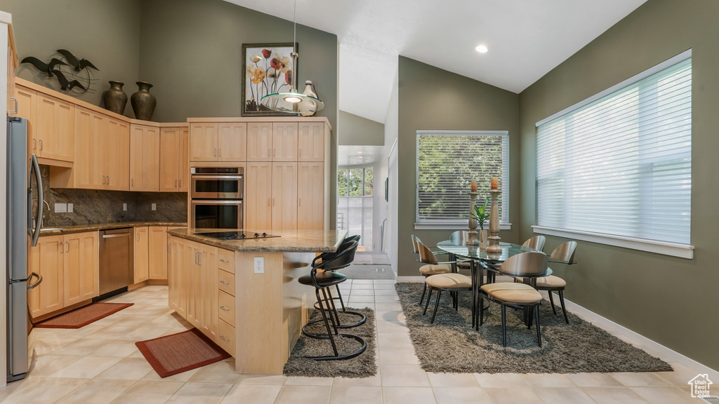 Kitchen featuring stainless steel appliances, light brown cabinets, a center island, dark stone countertops, and decorative backsplash