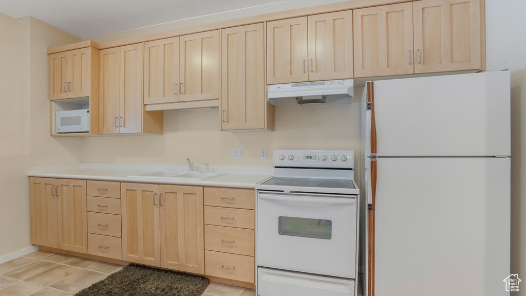 Kitchen with white appliances, light brown cabinets, under cabinet range hood, a sink, and light countertops