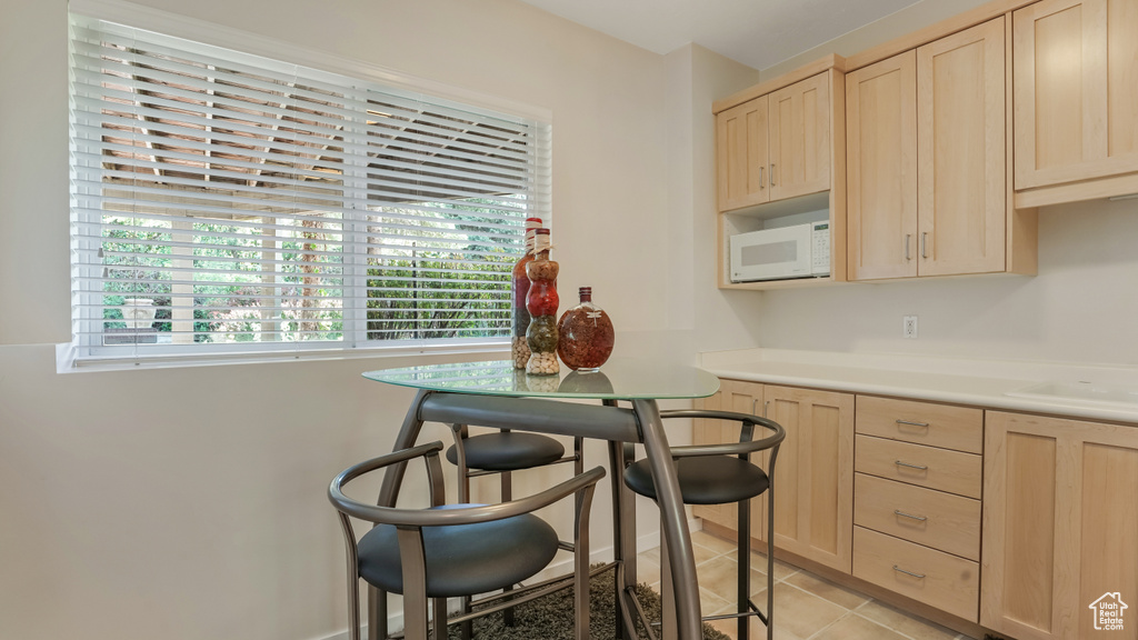 Kitchen featuring light brown cabinets, white microwave, light countertops, and light tile patterned floors