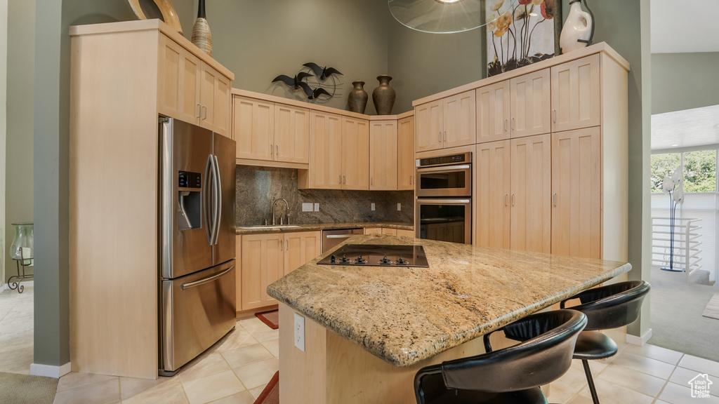 Kitchen featuring stainless steel appliances, light brown cabinets, a kitchen island, light tile patterned flooring, and a high ceiling