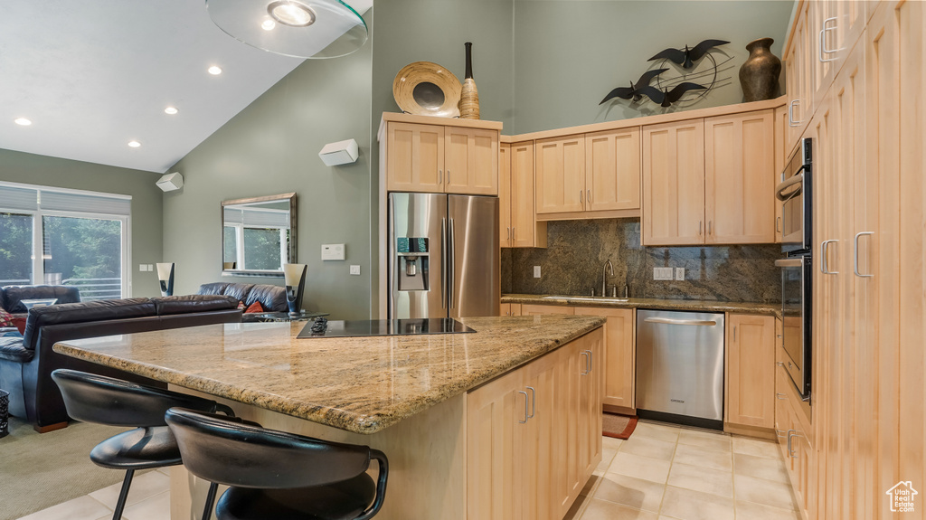 Kitchen with appliances with stainless steel finishes, light brown cabinetry, high vaulted ceiling, a sink, and open floor plan