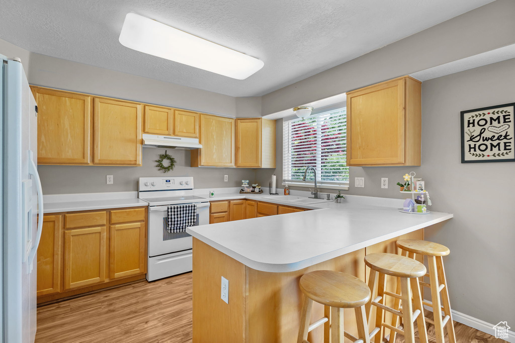 Kitchen featuring white appliances, under cabinet range hood, a sink, a peninsula, and a breakfast bar area