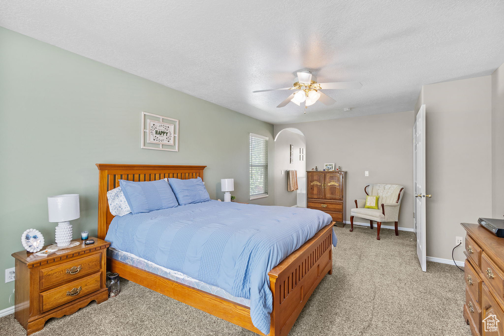 Bedroom featuring baseboards, arched walkways, light colored carpet, a ceiling fan, and a textured ceiling
