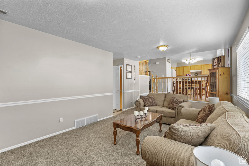Living room featuring a chandelier, light carpet, baseboards, a textured ceiling, and healthy amount of natural light