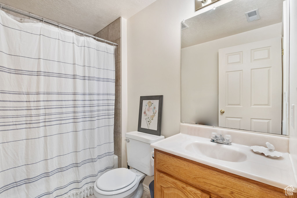 Full bath featuring vanity, toilet, a textured ceiling, and curtained shower