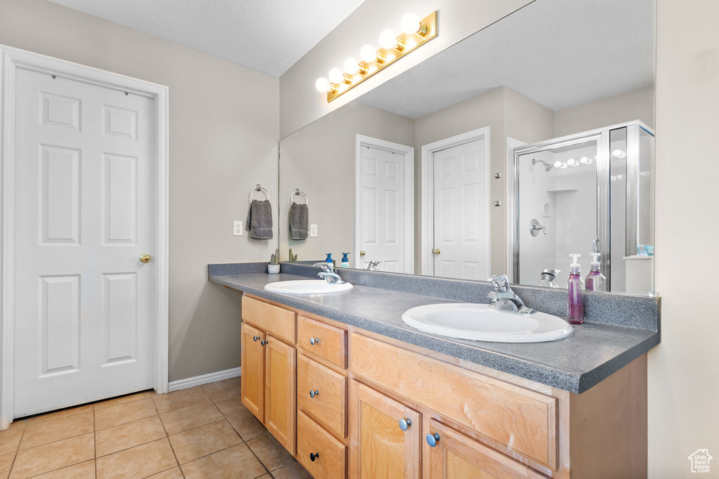 Bathroom featuring tile patterned floors, a shower stall, double vanity, and baseboards