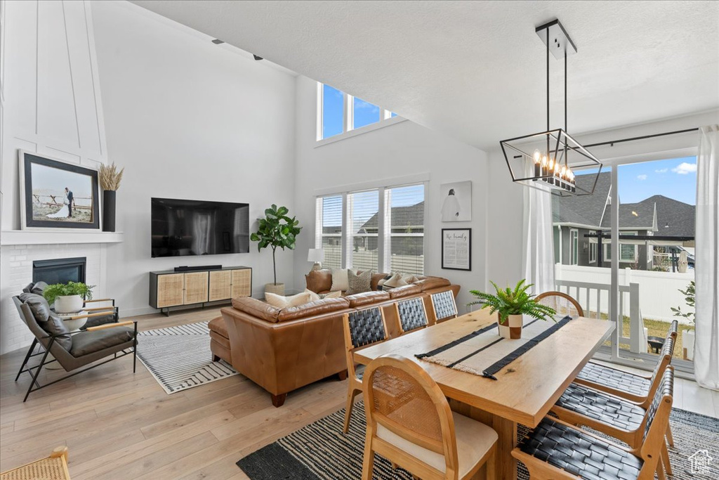 Dining room with a chandelier, light wood-type flooring, a brick fireplace, and a towering ceiling