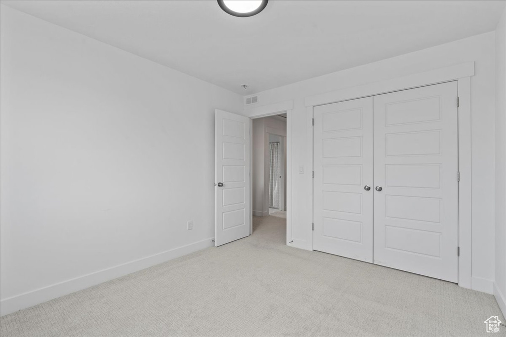 Unfurnished bedroom featuring light carpet, baseboards, and a closet