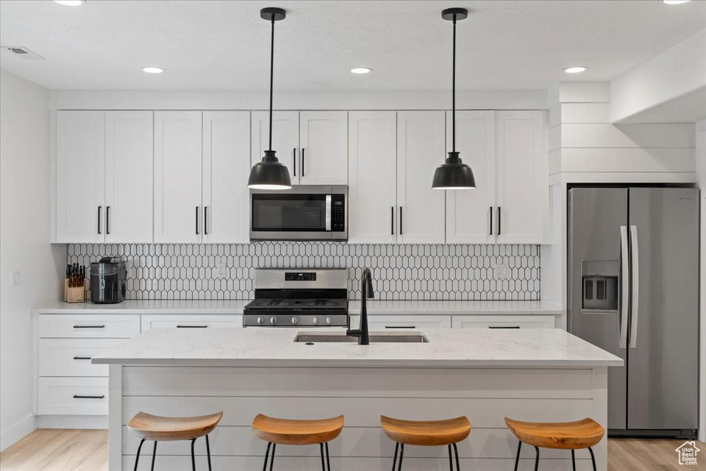 Kitchen featuring appliances with stainless steel finishes, a sink, a breakfast bar area, white cabinetry, and recessed lighting