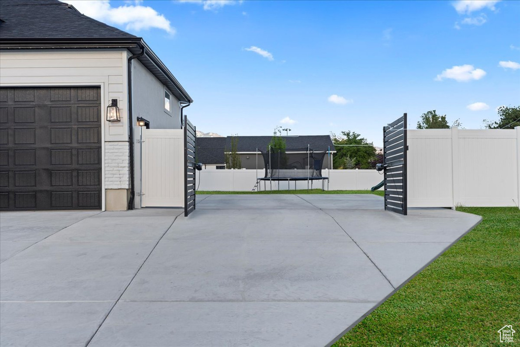 View of side of home with a trampoline, fence, a garage, and concrete driveway