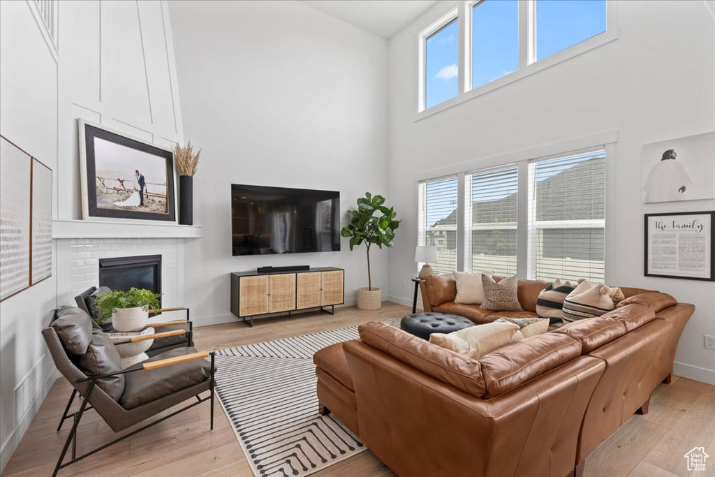 Living room with a high ceiling, light wood-style floors, a brick fireplace, and baseboards