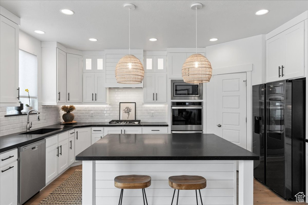 Kitchen featuring appliances with stainless steel finishes, a sink, dark countertops, white cabinets, and backsplash