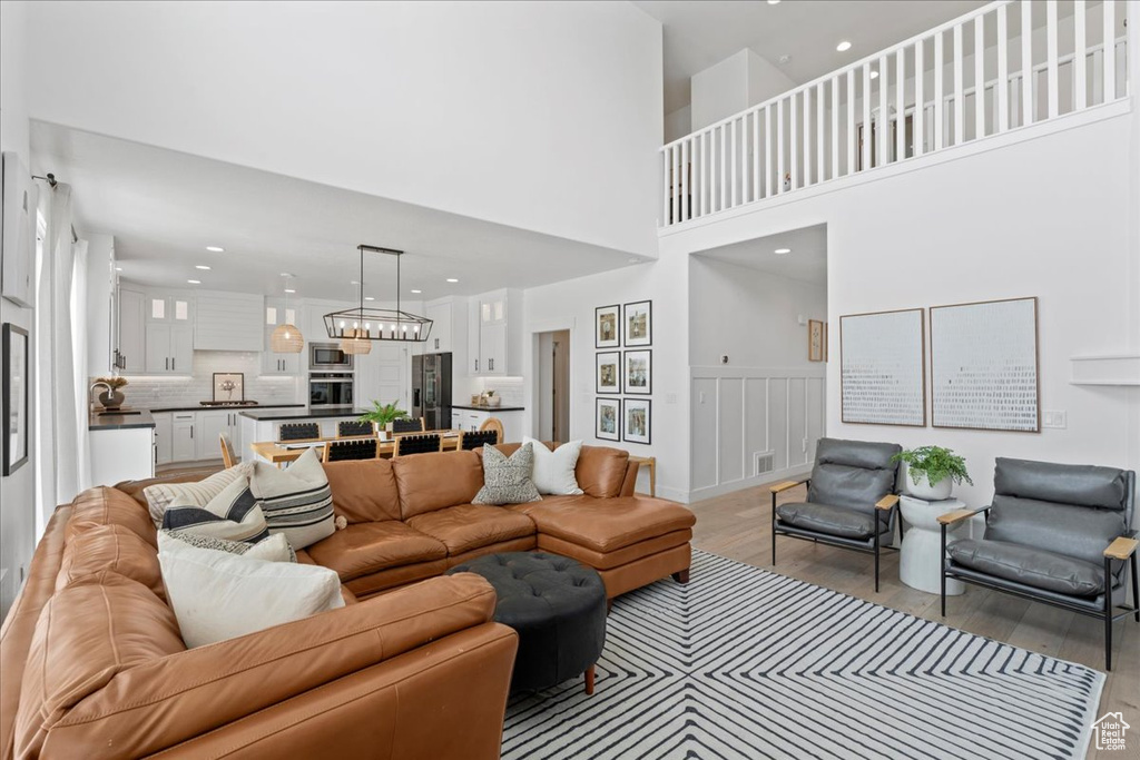 Living room featuring light wood-style flooring, a chandelier, recessed lighting, wainscoting, and a decorative wall