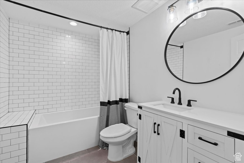 Full bath featuring toilet, vanity, tile patterned floors, shower / tub combo with curtain, and a textured ceiling