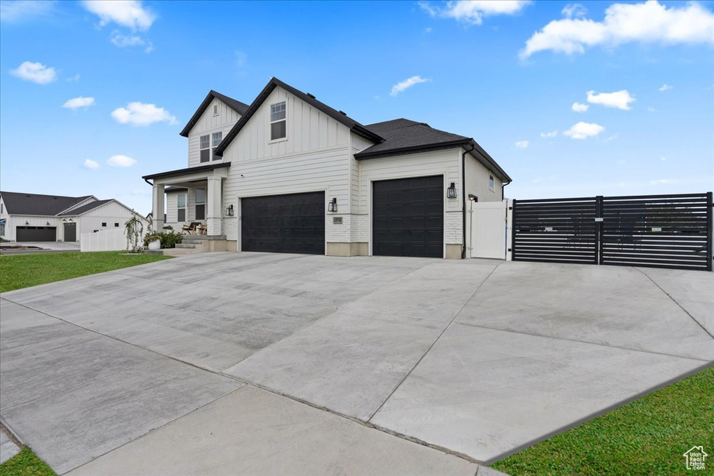 View of front of home with board and batten siding, a gate, driveway, a garage, and fence