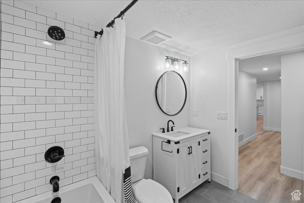 Full bath featuring shower / bath combo, toilet, a textured ceiling, vanity, and wood finished floors