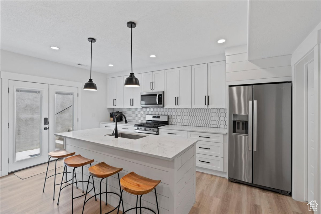 Kitchen with appliances with stainless steel finishes, a sink, a center island with sink, tasteful backsplash, and white cabinetry