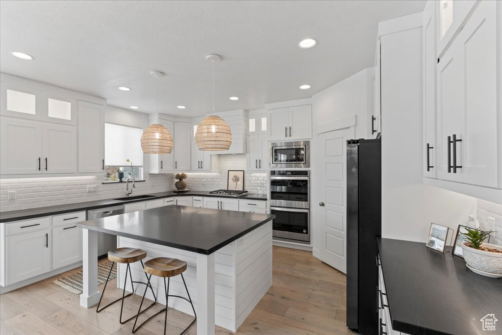 Kitchen with stainless steel appliances, dark countertops, a sink, a kitchen bar, and recessed lighting
