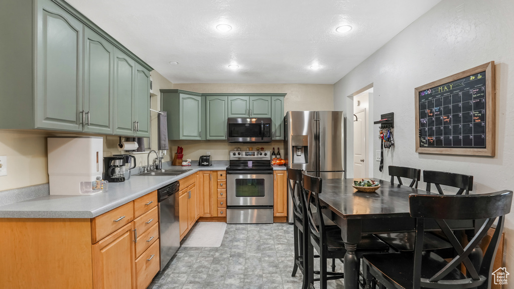 Kitchen with appliances with stainless steel finishes, a sink, green cabinets, light countertops, and recessed lighting