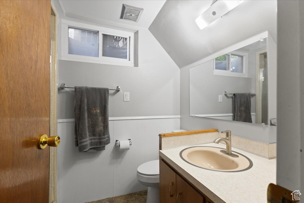 Bathroom featuring toilet, vaulted ceiling, vanity, wainscoting, and tile patterned floors