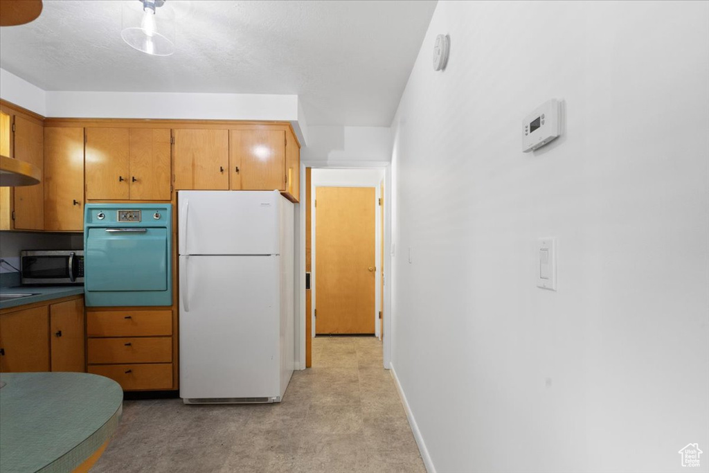 Kitchen with freestanding refrigerator, wall oven, stainless steel microwave, light colored carpet, and baseboards
