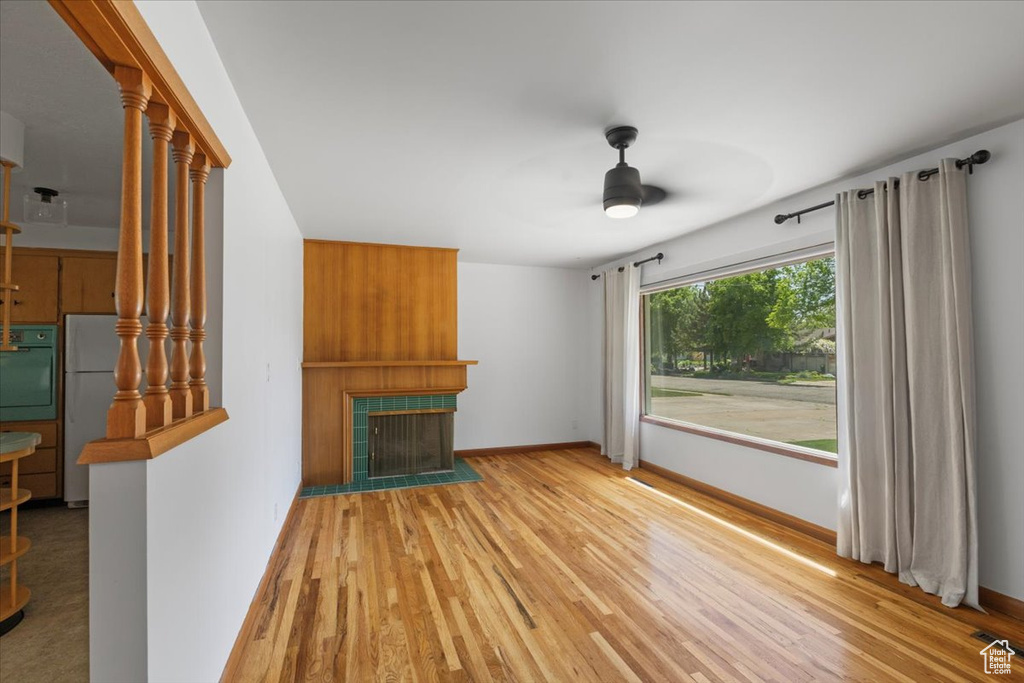 Unfurnished living room with ceiling fan, a tile fireplace, wood finished floors, and baseboards