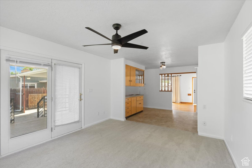 Unfurnished living room featuring ceiling fan, light carpet, and baseboards