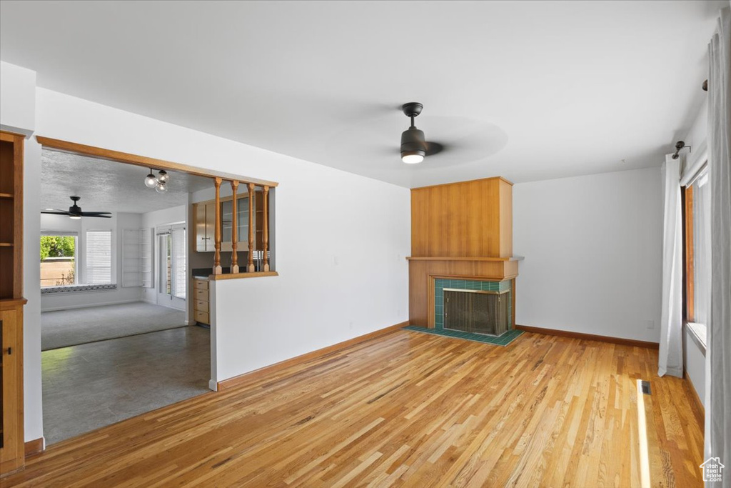 Unfurnished living room featuring a ceiling fan, a fireplace with raised hearth, and wood finished floors