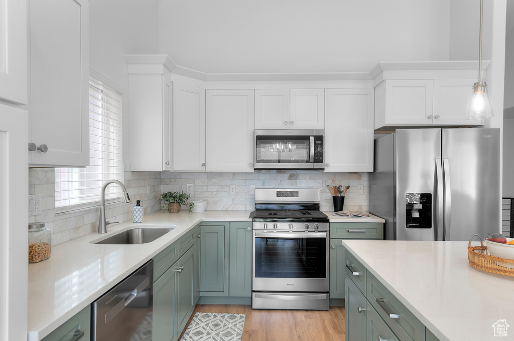 Kitchen featuring stainless steel appliances, a sink, light countertops, white cabinets, and backsplash
