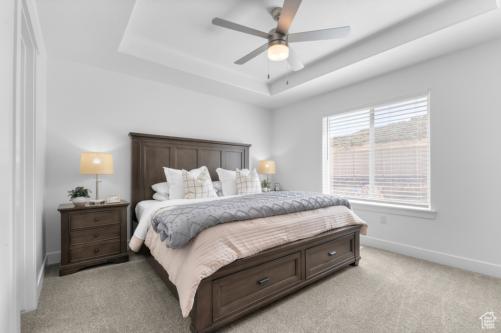 Bedroom featuring a raised ceiling, light colored carpet, baseboards, and ceiling fan