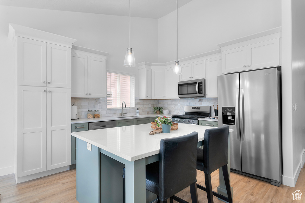 Kitchen featuring appliances with stainless steel finishes, a sink, light countertops, a towering ceiling, and decorative backsplash