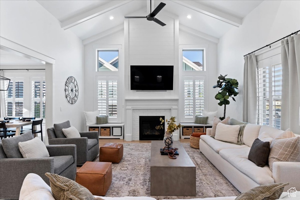 Living room featuring beamed ceiling, high vaulted ceiling, a ceiling fan, a fireplace, and wood finished floors