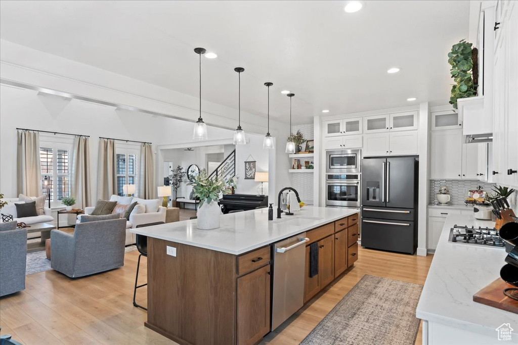 Kitchen with appliances with stainless steel finishes, a sink, light wood-style flooring, an island with sink, and white cabinetry