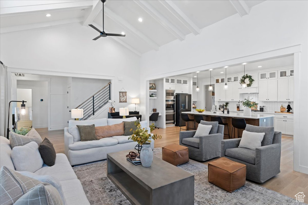 Living area featuring light wood finished floors, high vaulted ceiling, stairway, beam ceiling, and ceiling fan