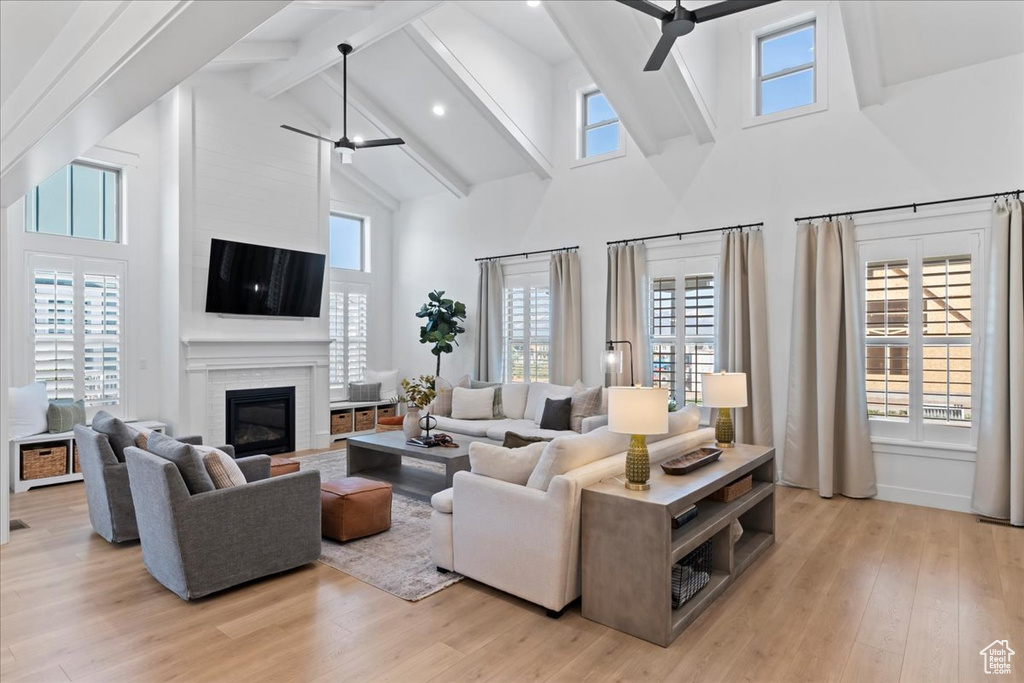 Living area featuring ceiling fan, high vaulted ceiling, beam ceiling, light wood-type flooring, and a fireplace