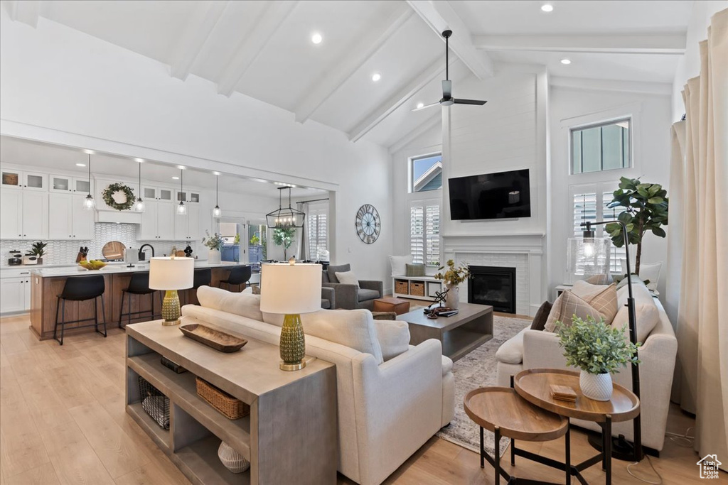 Living room featuring a glass covered fireplace, beamed ceiling, high vaulted ceiling, light wood finished floors, and recessed lighting