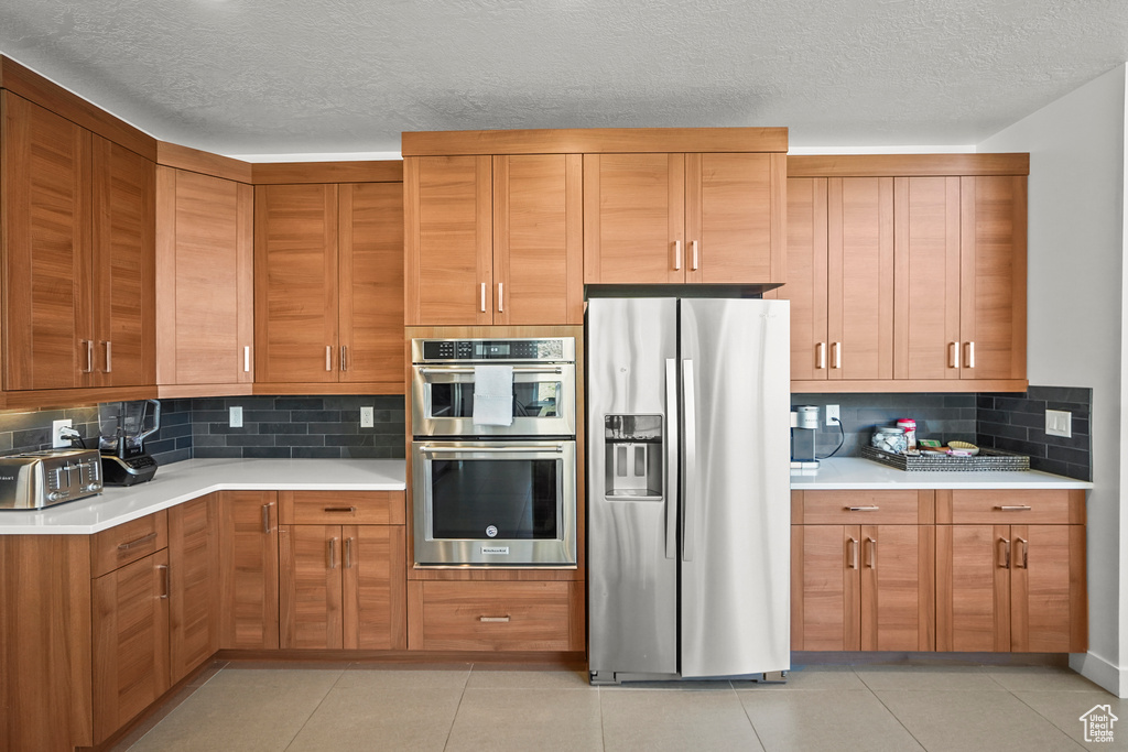 Kitchen with appliances with stainless steel finishes, light countertops, tasteful backsplash, a textured ceiling, and brown cabinets