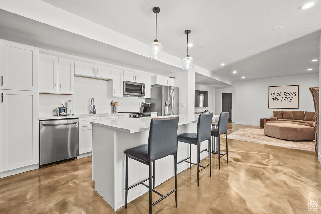 Kitchen with stainless steel appliances, finished concrete flooring, a kitchen breakfast bar, recessed lighting, and white cabinets