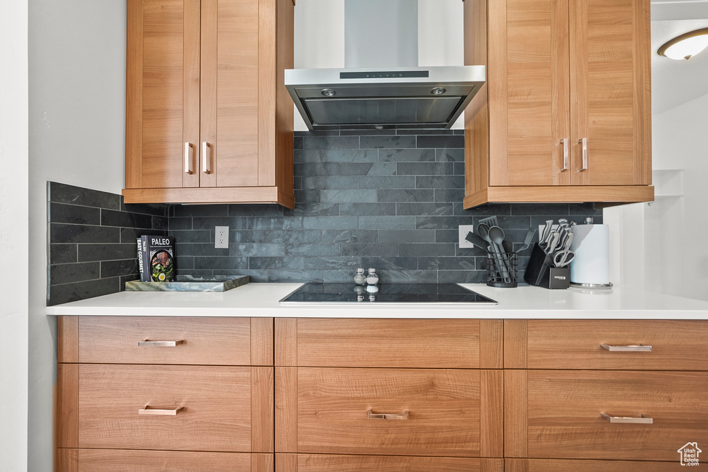 Kitchen with exhaust hood, black electric stovetop, backsplash, and light countertops