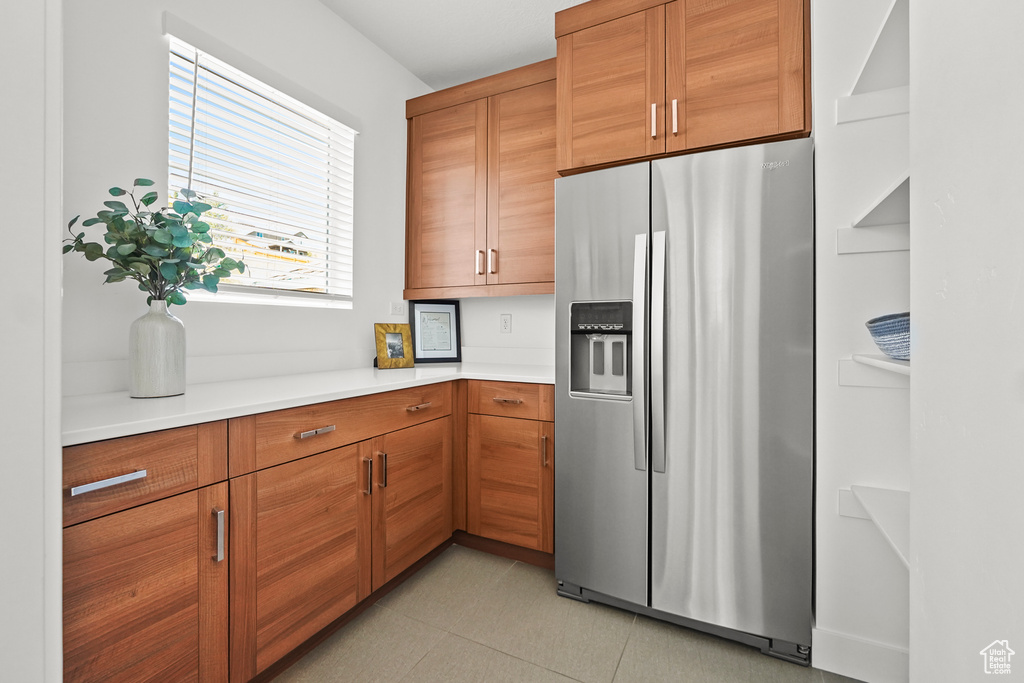 Kitchen featuring stainless steel refrigerator with ice dispenser, light countertops, brown cabinetry, and light tile patterned floors